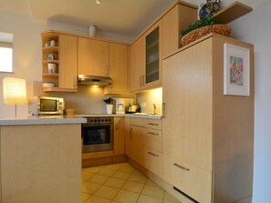 A compact kitchen with wooden cabinets, a microwave, an oven, and a sink. - Residence Starfish Whg S-10 .. - See-10 (Kühlungsborn)