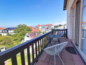 Ein Balkon mit Tisch und Stühlen, mit Blick auf ein Wohngebiet mit roten Dächern und einem Riesenrad in der Ferne.