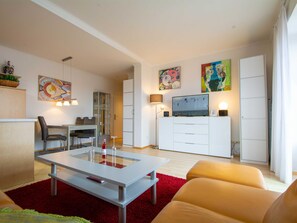A modern living room with a glass-top coffee table, a sofa, a dining area with chairs, a TV, and artwork on the walls. - Residence Starfish Whg S-10 .. - See-10 (Kühlungsborn)