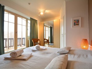 Habitación de hotel con dos camas, un ventanal grande, una silla y una lámpara.