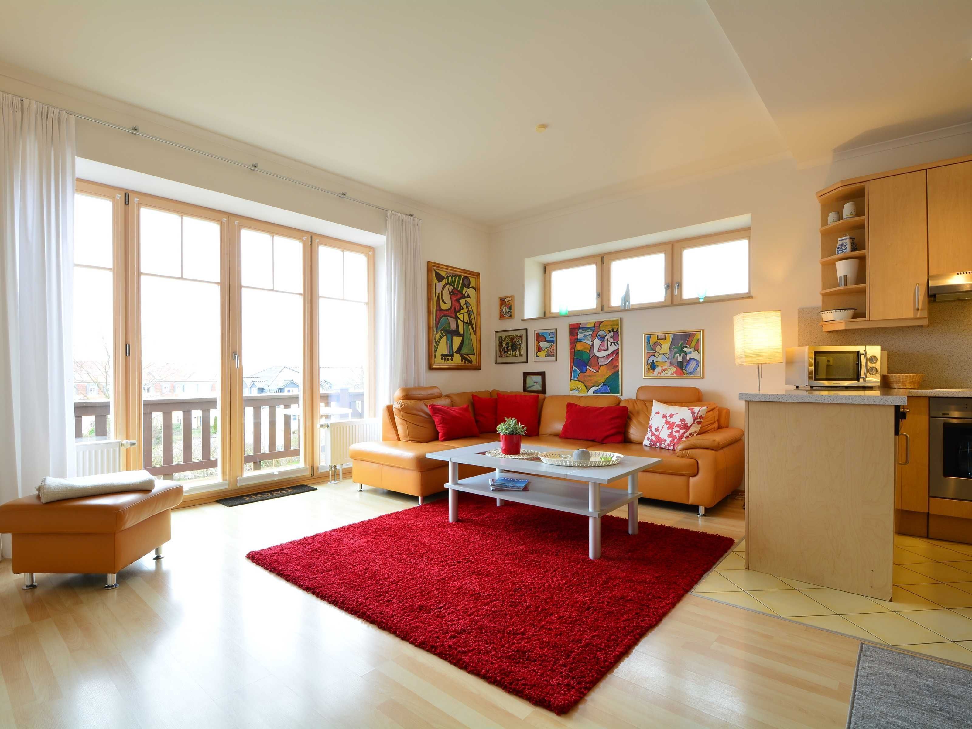 A spacious living room with a red rug, a sofa set, a coffee table, and a kitchen area with a microwave and oven.