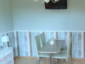 A dining area with a table, chairs, a lamp, and a television mounted on the wall. - Lod - Goldbach - Holiday apartment (Loddin)