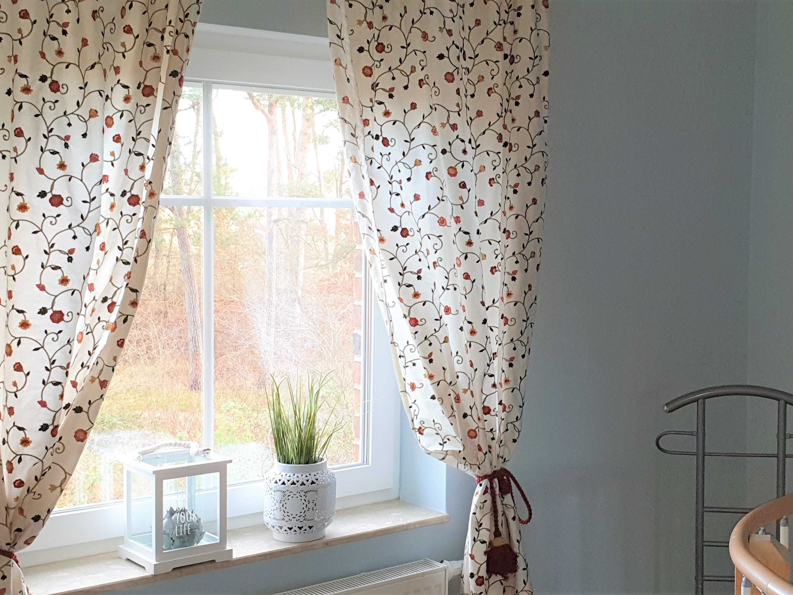 A window with floral curtains, a potted plant, and a small framed picture on the windowsill.