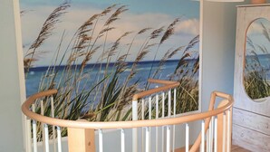 A staircase with a railing, a wall with a beach scene mural, and a cabinet with a mirror. - Lod - Goldbach - Holiday apartment (Loddin)