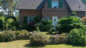 A two-story stone house with a tiled roof, green shutters, and a garden with various plants and flowers. - Lod - Goldbach - Holiday apartment (Loddin)