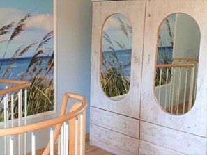 A room with a wooden staircase, a white cabinet with circular mirrors, and a mural of a beach scene. - Lod - Goldbach - Holiday apartment (Loddin)