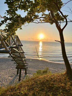 A beach with a metal staircase leading to a wooden deck, overlooking the sea at sunset. - Lod - Goldbach - Holiday apartment (Loddin)