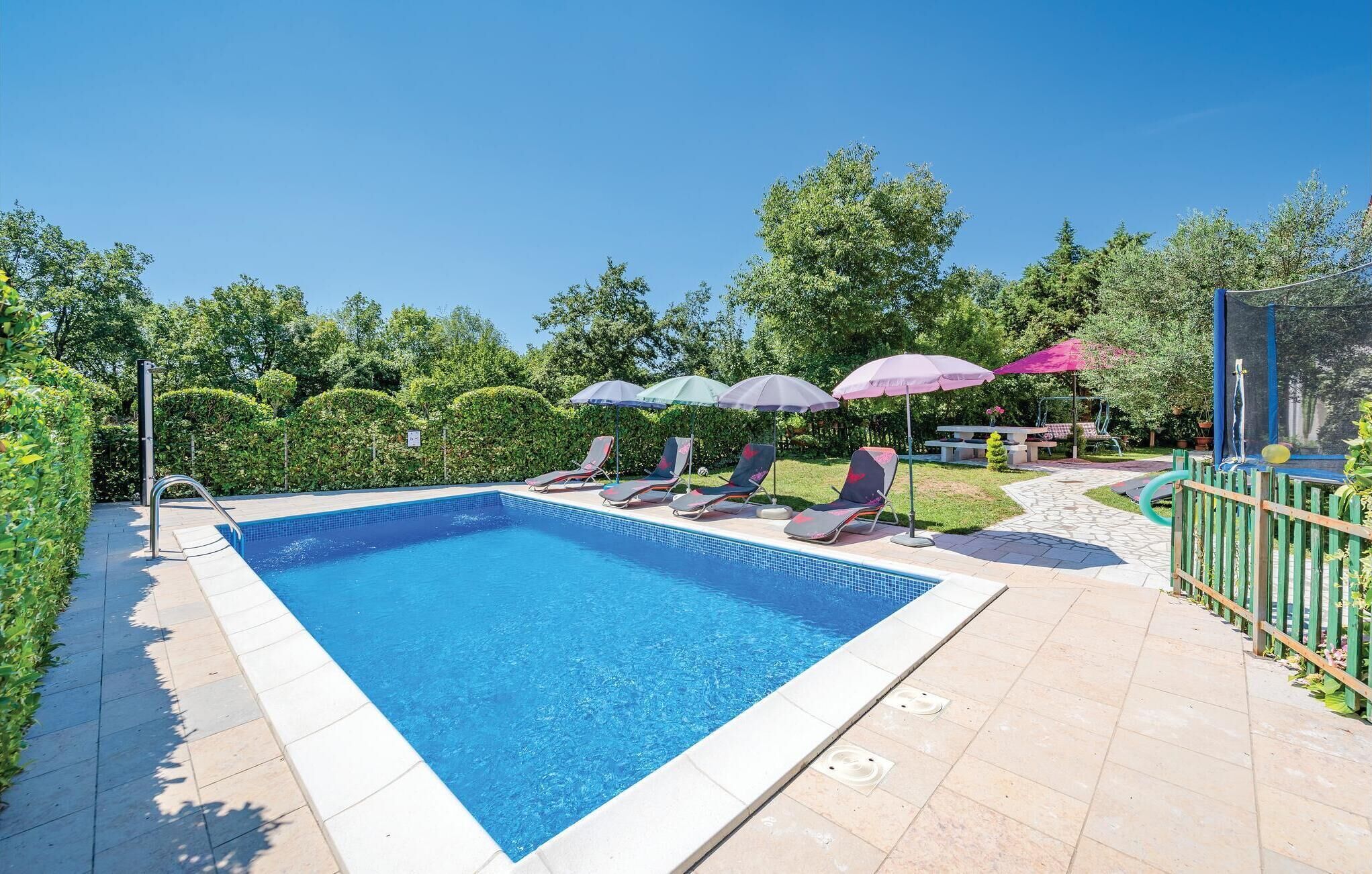 Une piscine rectangulaire dont le bord est recouvert de carrelage, entourée de chaises longues et de parasols.