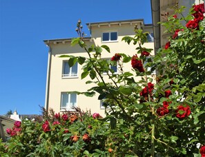 A building with multiple windows and balconies, surrounded by lush greenery and red flowers. - Metropol Whg. ME-08. - Metropol Whg. 08 (Kühlungsborn)
