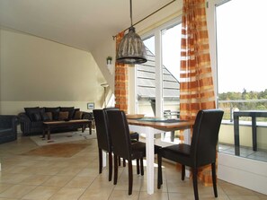 Un comedor con una mesa y sillas de vidrio, una lámpara colgante y vistas a un balcón con barandilla.