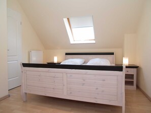 A bedroom with a sloped ceiling, a skylight, a bed with a wooden frame, two bedside tables with lamps, and a radiator.