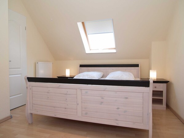 Ein Schlafzimmer mit schrägen Wänden, einem Oberlicht, einem Bett mit Holzrahmen, zwei Nachttischen mit Lampen und einer Heizung.