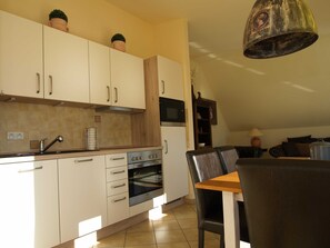 Eine moderne Küche mit weißen Schränken, einem eingebauten Ofen und einem Essbereich mit Tisch und Stühlen.