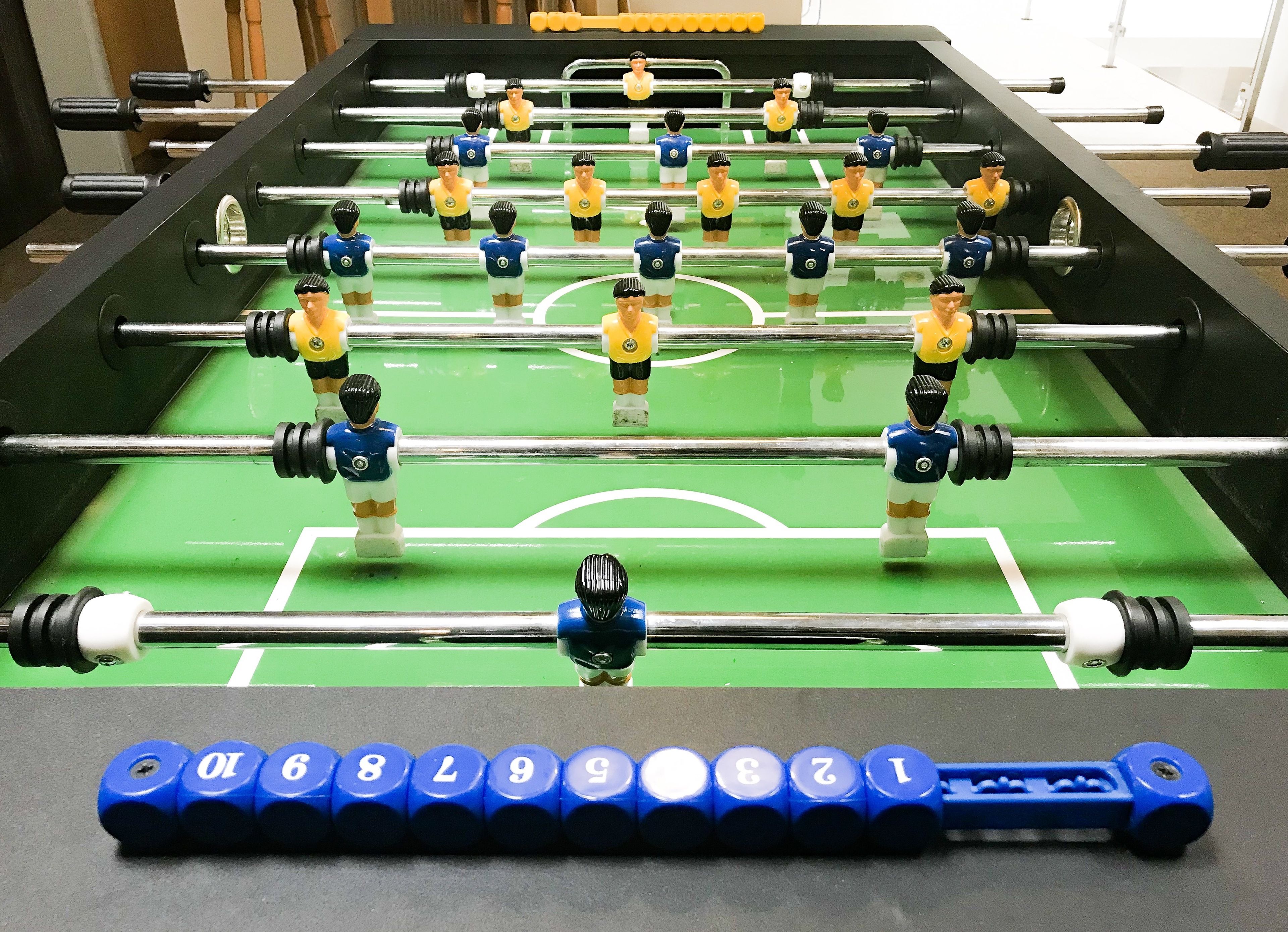 Een tafelvoetbaltafel met een groene speeloppervlak en blauwe en gele spelerfiguren.