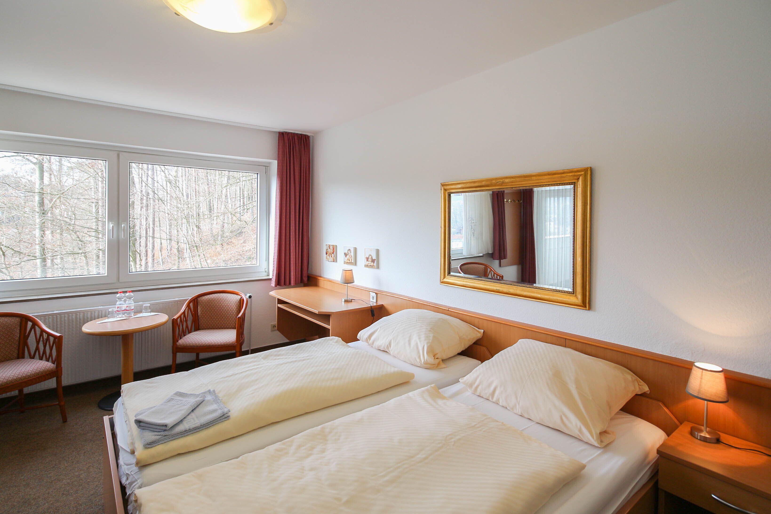 Habitación de hotel con dos camas, un escritorio, una silla, una mesita y una ventana con cortinas.