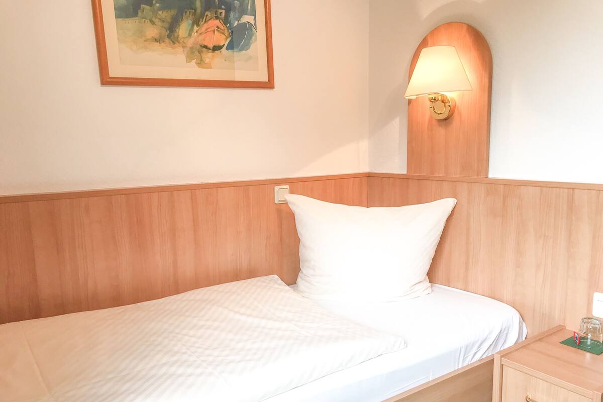 A neatly made bed with a wooden headboard, a bedside table with a lamp, and a framed painting on the wall.