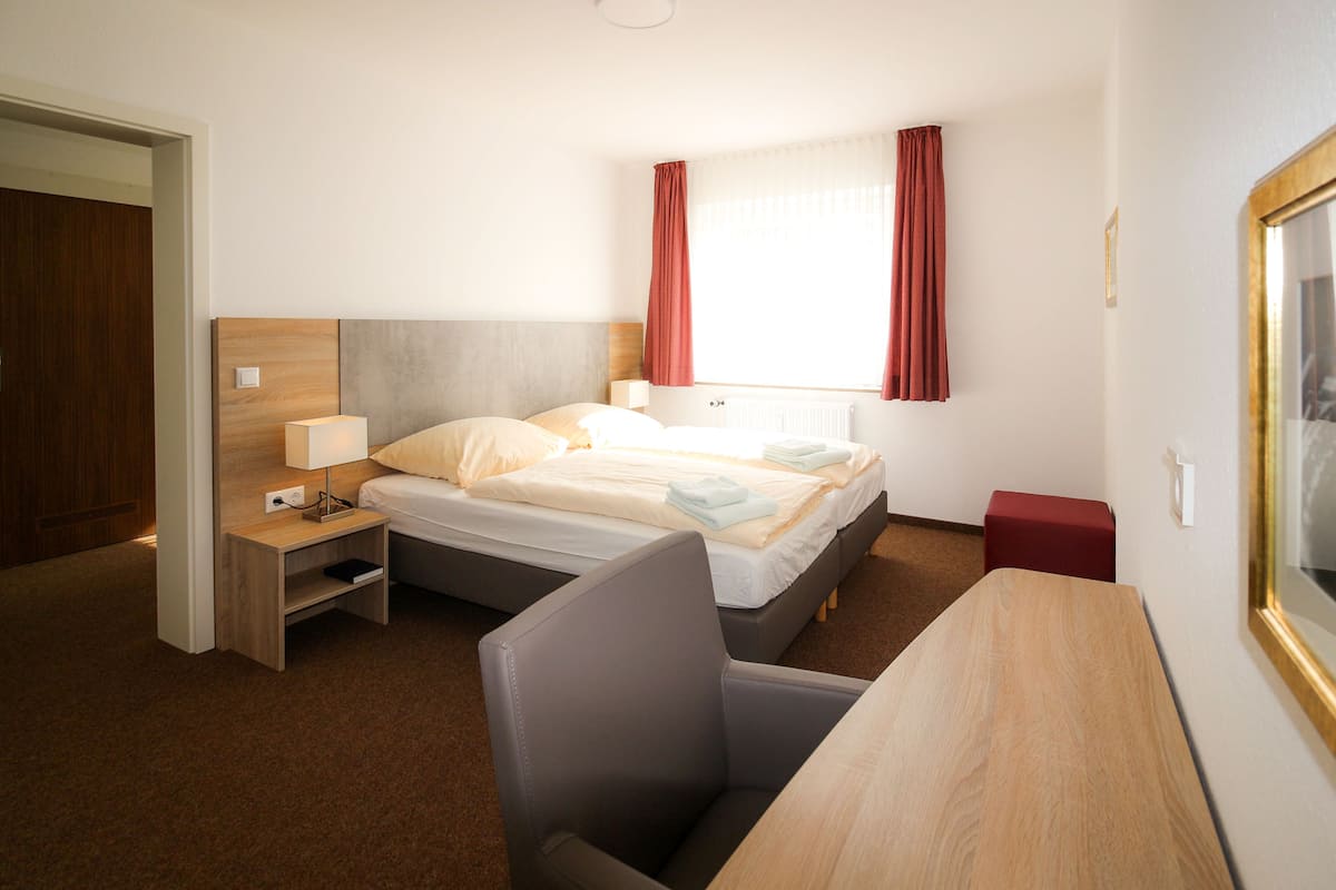 A hotel room with a bed, bedside table, lamp, chair, and a small table.