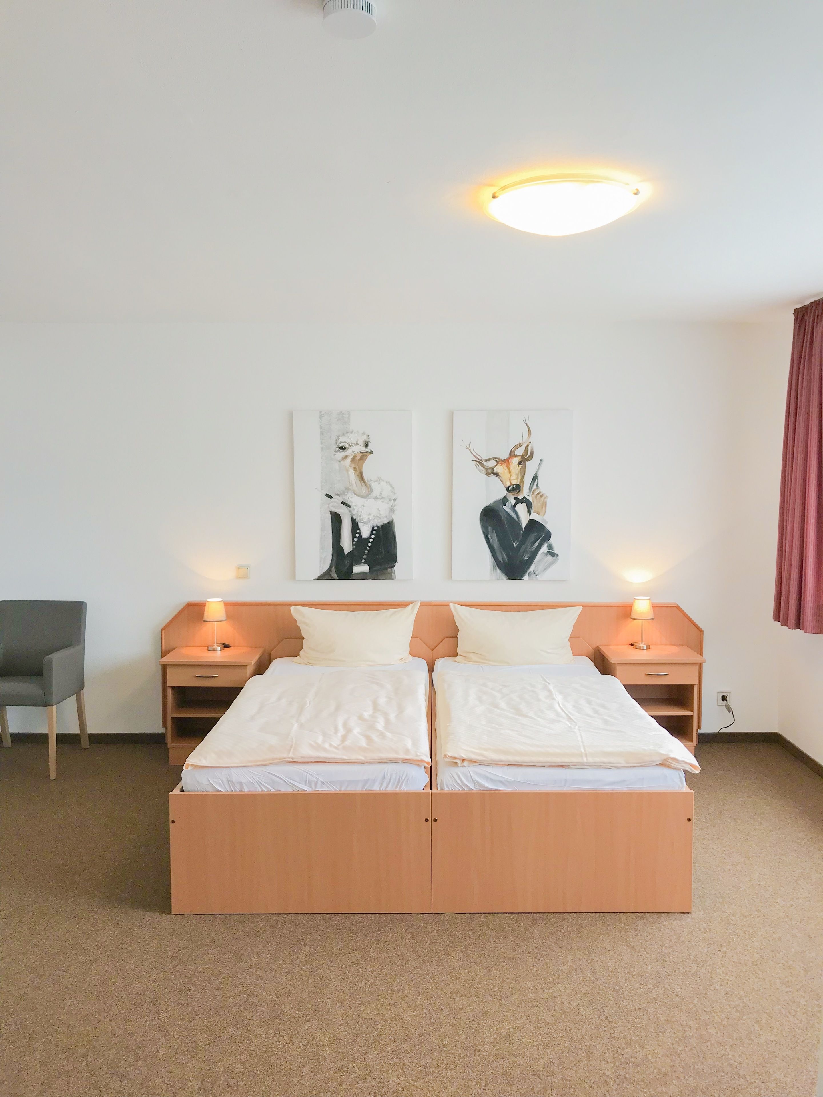 Una cama doble con dos mesitas de noche, una silla y dos obras de arte colgadas en la pared.