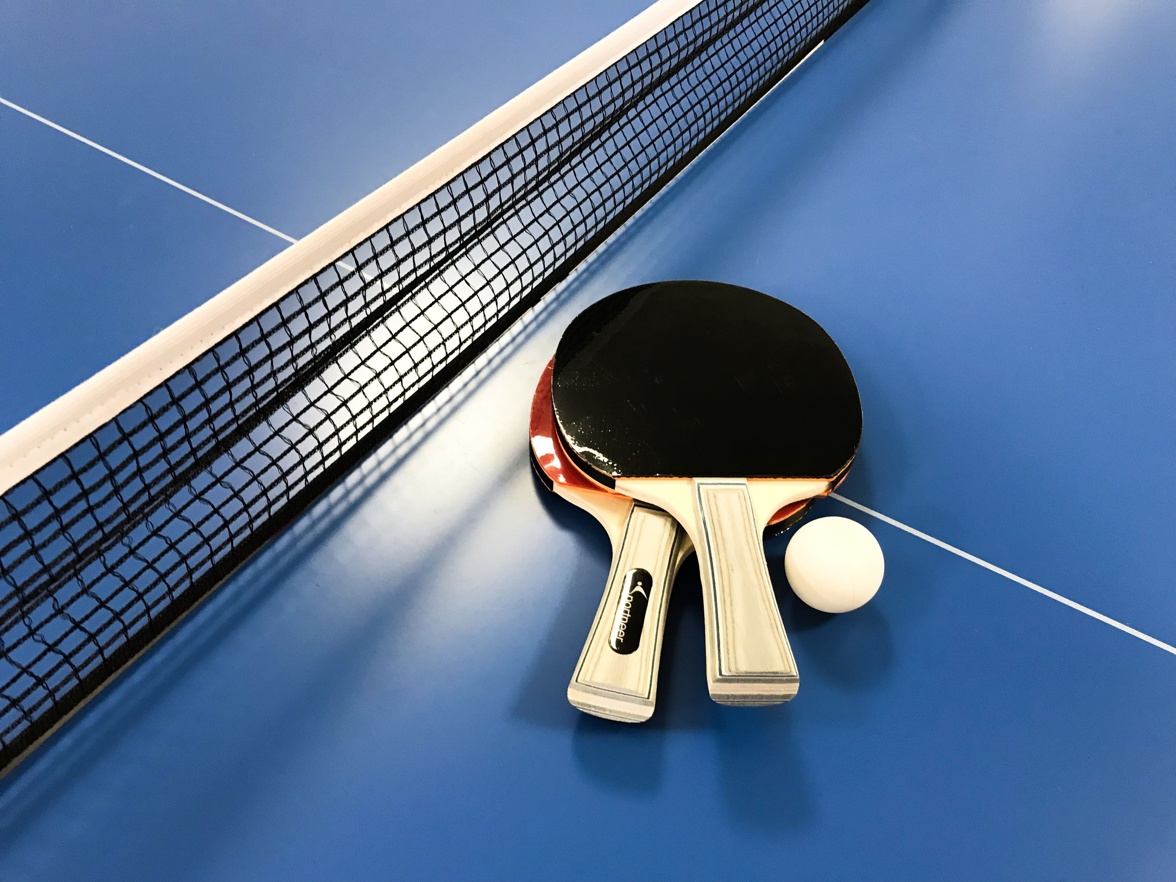 Une table de ping-pong avec un filet, deux raquettes et une balle, le tout posé sur une surface bleue.