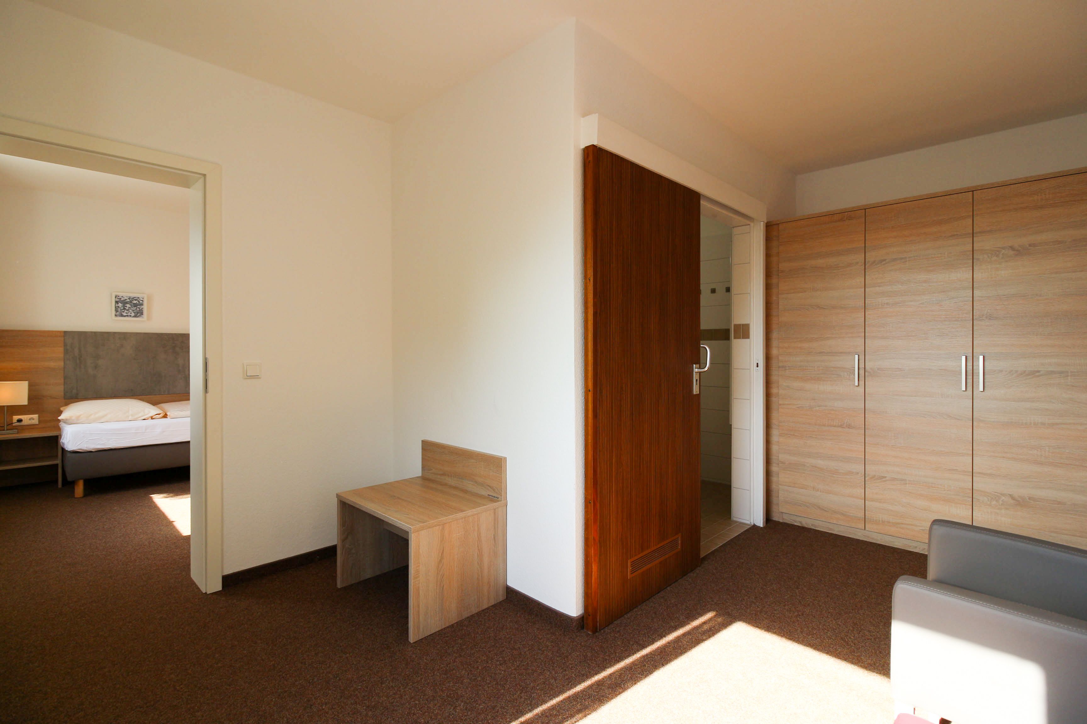 Une chambre d’hôtel moderne comprenant un lit, une armoire en bois, un petit banc en bois et un bureau.