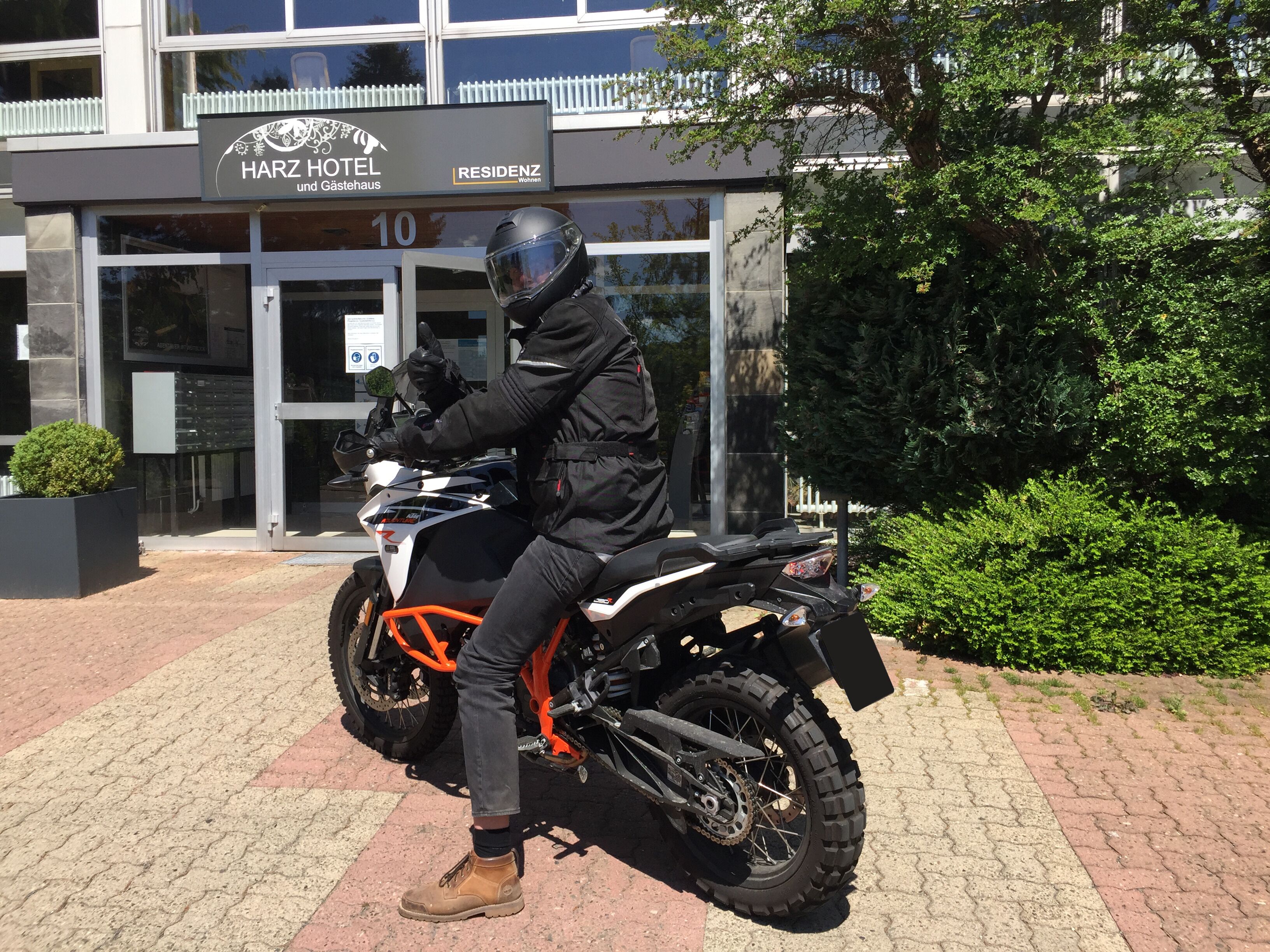 A person on a motorcycle in front of a building with a sign reading "HARZ HOTEL und Gästehaus".