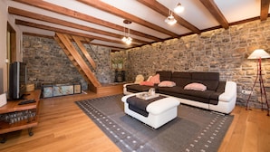 A cozy living room with a stone wall, wooden beams, a sofa, and a television. - Gorgeous home in Poljane with sauna (Poljane)