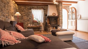A cozy living room with a stone wall, a fireplace, a sofa, and a dining table. - Gorgeous home in Poljane with sauna (Poljane)