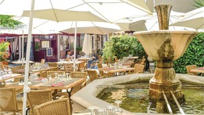 Een buitenterras met rieten tafels en stoelen, een fontein in het midden en parasols voor schaduw.