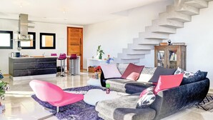 Een moderne woonkamer met een grijze bank, een roze fauteuil en een trap.