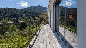 Een houten terras met glazen balustrade met uitzicht op een bergachtig landschap.
