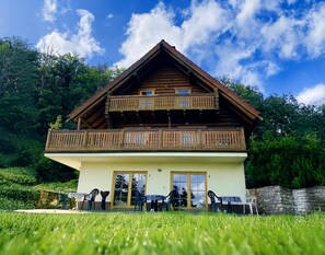Eine zweistöckige Holzhütte mit Balkon, einer Glastür und Sitzgelegenheiten im Freien.