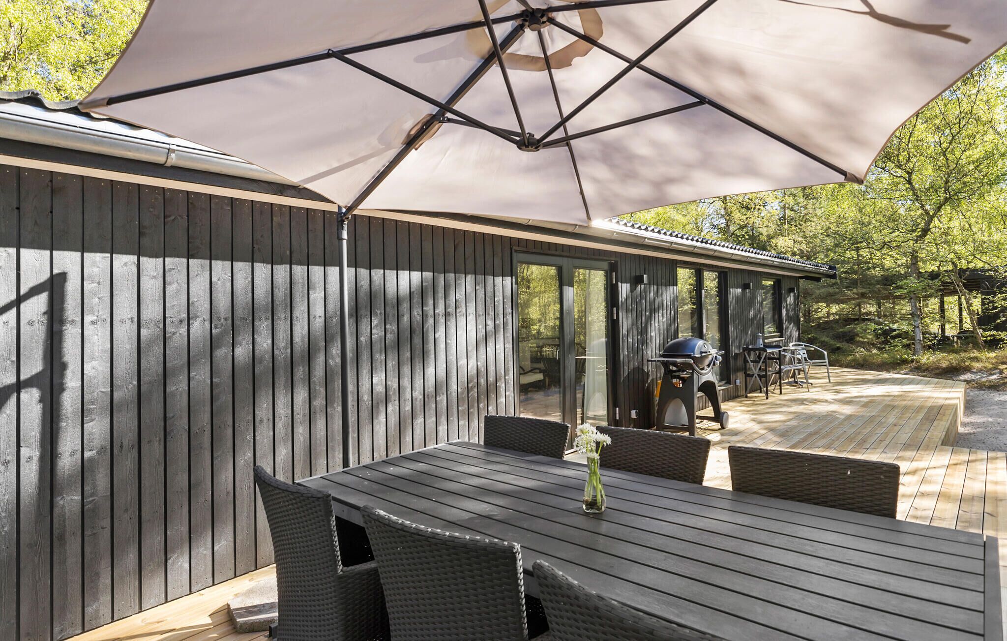 An outdoor patio with a wooden table and chairs, a grill, and a covered area with a large umbrella.