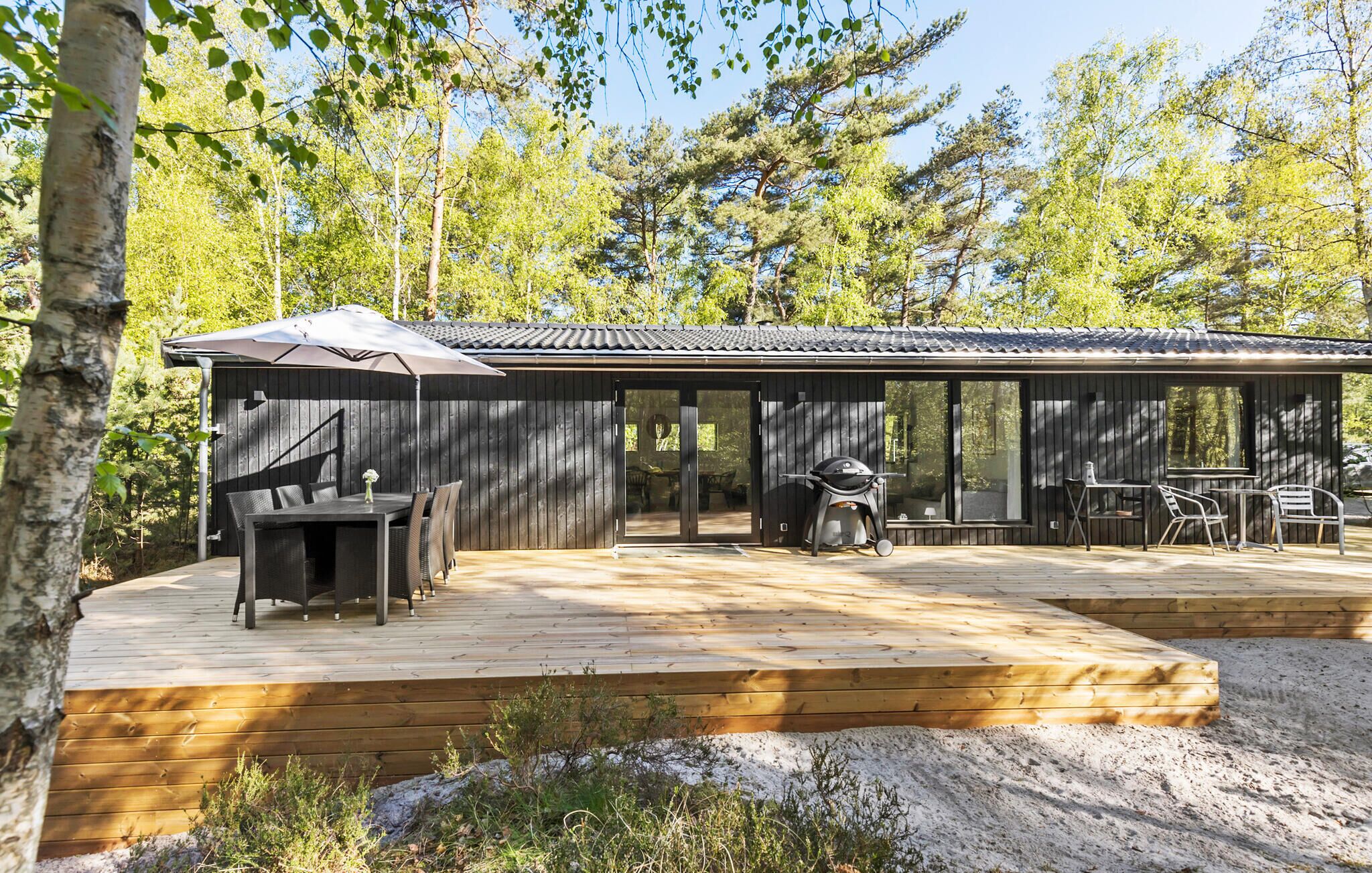Eine Holzhütte mit einer Terrasse, Sitzgelegenheiten im Freien und einem Grill.