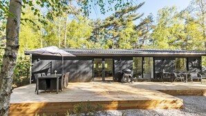 Une cabane en bois dotée d’une terrasse, d’un espace salon extérieur et d’un barbecue.