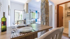 Un comedor con una mesa de madera dispuesta para dos personas, una botella de vino y vista a un baño con ducha y perchero.