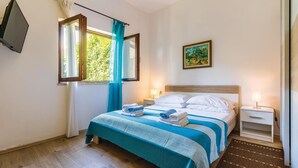 Una cama bien tendida con ropa de cama azul y blanca, una mesita de noche pequeña con una lámpara y un cuadro en la pared.