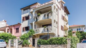 Un edificio residencial de varios pisos con balcones, un muro de piedra en primer plano y cielo despejado.