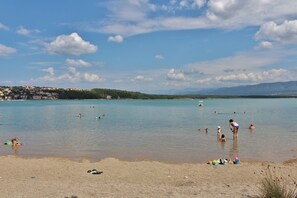 Una spiaggia con persone che nuotano e prendono il sole, cielo sereno e montagne in lontananza.
