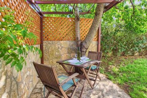 Un'area salotto all'aperto con tavolo e sedie, circondata da una pergola in legno e un muro in pietra.
