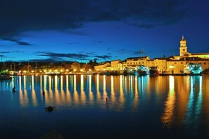 Paesaggio urbano sul lungomare di notte, con edifici illuminati che si riflettono in acque calme.