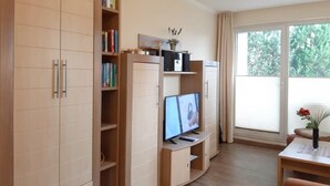 Ein modernes Wohnzimmer mit integriertem Fernseher, Holzschränken und einem großen Fenster mit Vorhängen.