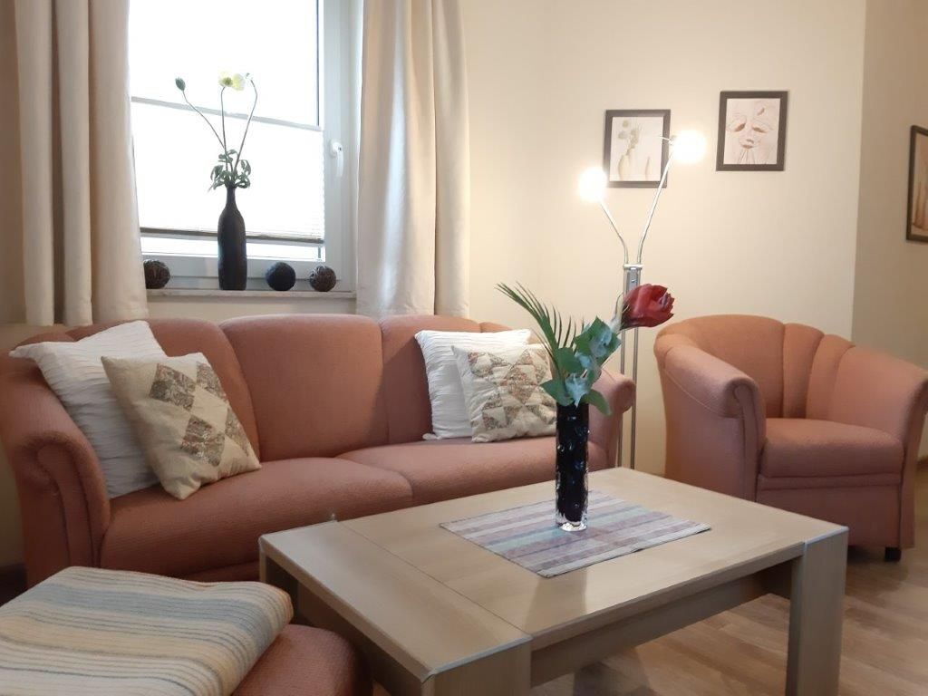 A living room with a sofa, a coffee table, and a vase with flowers.