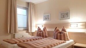 Ein Doppelbett mit gestreifter Bettwäsche, ein Nachttisch, ein Heizkörper und zwei gerahmte Bilder an der Wand.