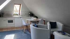 A modern kitchen with white cabinets, a dining area with a table and chairs, and a large window providing natural light. - Apartment 3 Shell - House Birkenallee / Reckleben GM 69705 (Graal-Müritz)