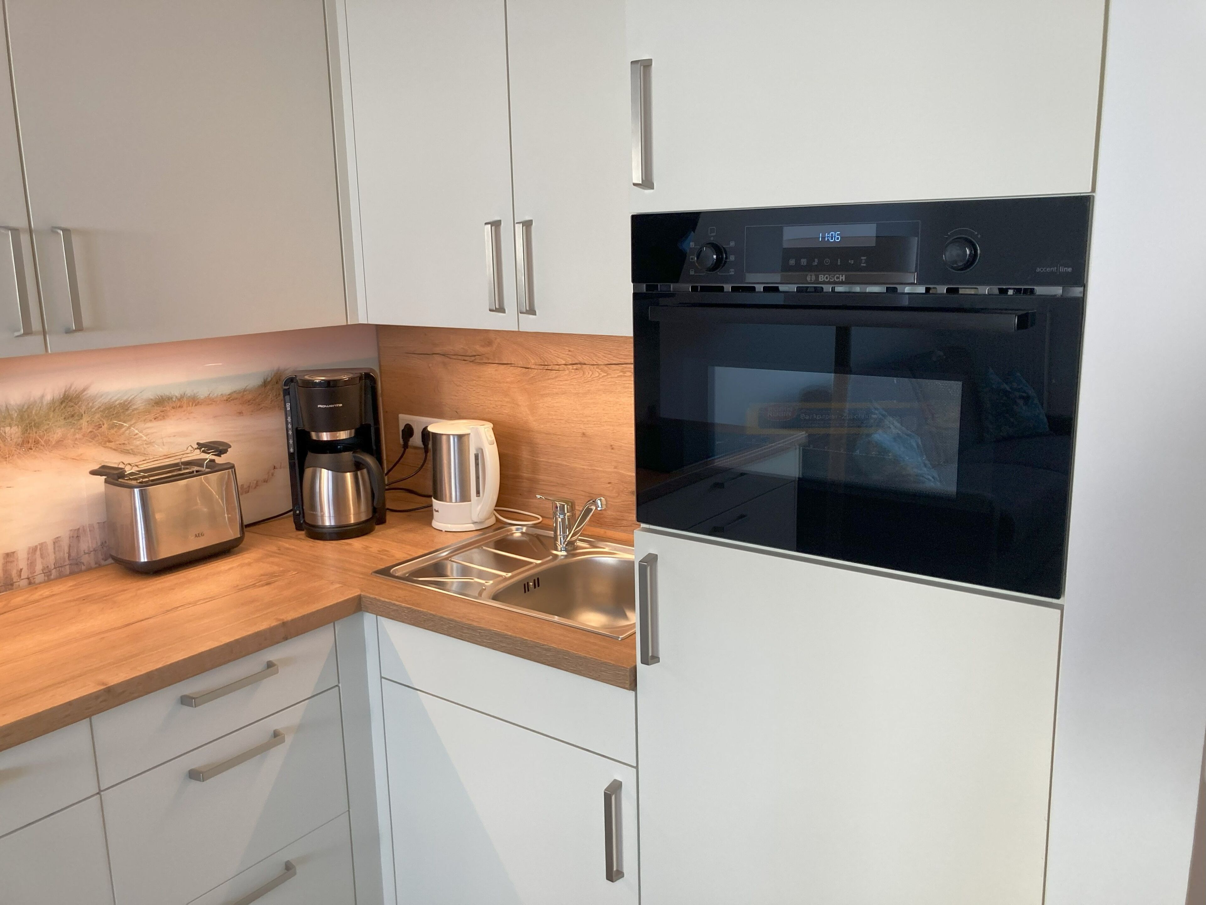 Una cocina moderna con armarios blancos, un tostador de acero inoxidable, una cafetera y un horno.