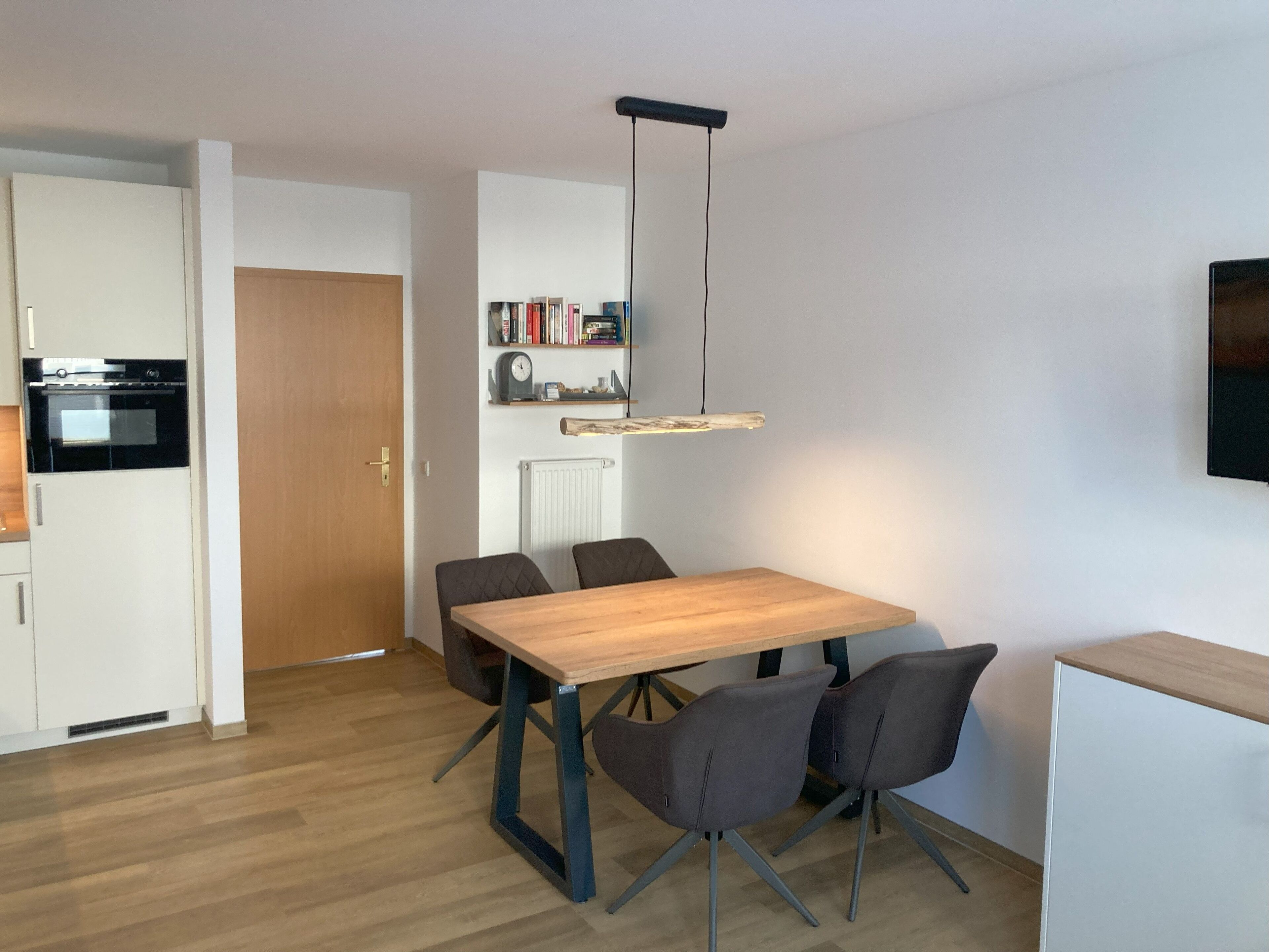 A modern kitchen with white cabinets, a black oven, and a wooden dining table with four chairs.