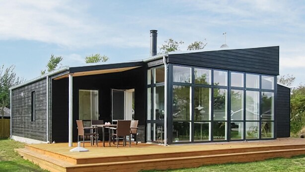 Une maison moderne dotée d’une terrasse, de grandes fenêtres et d’une cheminée.
