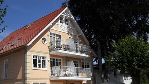 A two-story building with a red-tiled roof, white-framed windows, and balconies with metal railings. - Dünenstr. 3a Whg.Ki-01. - Ki-Whg. 01 (Kühlungsborn)