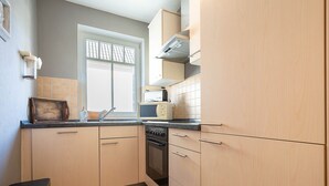 A compact kitchen with light wood cabinets, a black countertop, and a window with a view. - Dünenstr. 3a Whg.Ki-01. - Ki-Whg. 01 (Kühlungsborn)
