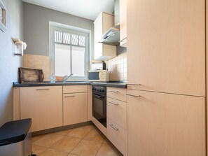 Uma cozinha compacta com armários de madeira clara, bancada preta e janela com vista.